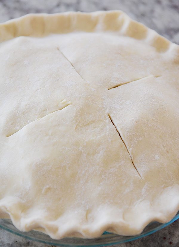 Top view of an uncooked pie crust with four slits in it.