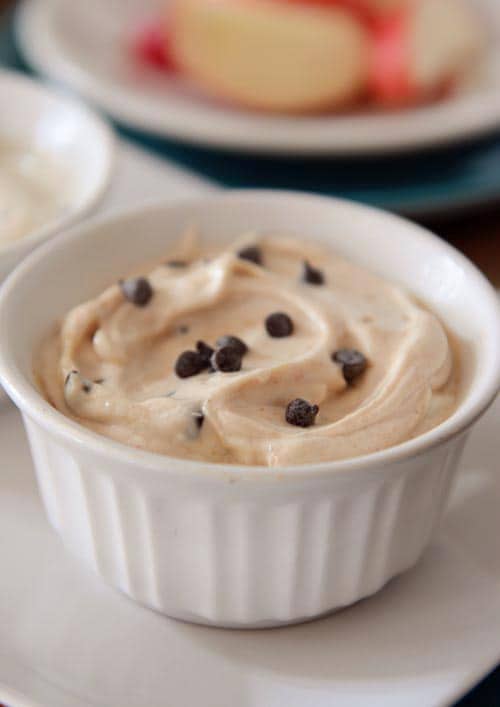 A small white ramekin full of cookie dough tipped with mini chocolate chips sprinkled on top.