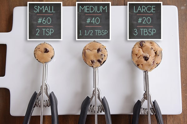 Small, medium, and large cookie scoops filled with raw cookie dough.