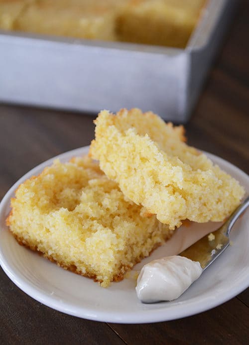 white plate with a split piece of cornbread and a knife with butter on the side