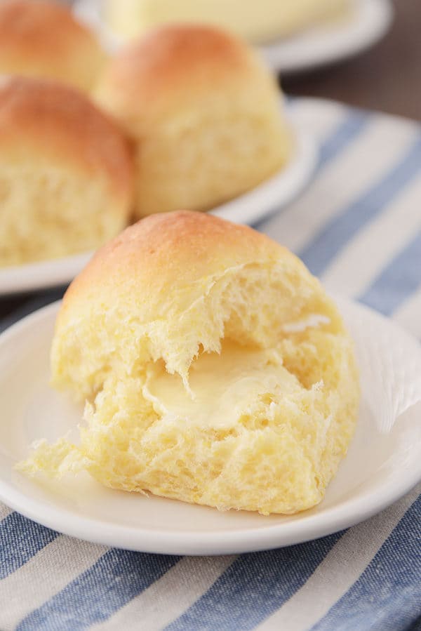A cornmeal roll split in half with a pat of butter in the middle.
