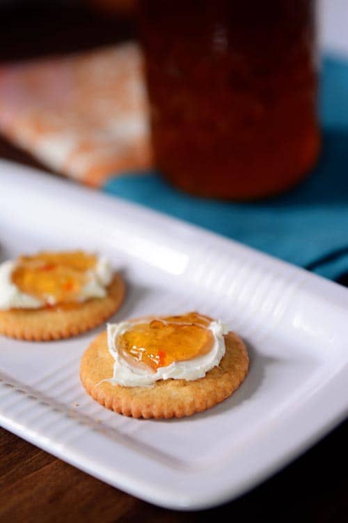 Ritz crackers on a white platter topped with cream cheese and jalapeno jelly.