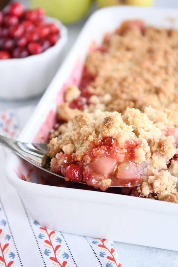 Scoop of cranberry pear crumble in white baking pan.