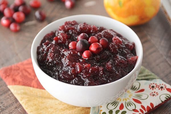 A white bowl of homemade cranberry sauce topped with a few fresh cranberries.