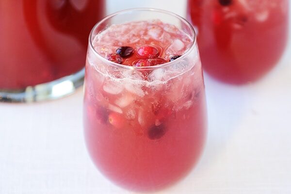 A clear glass full of red punch and floating cranberries on top.