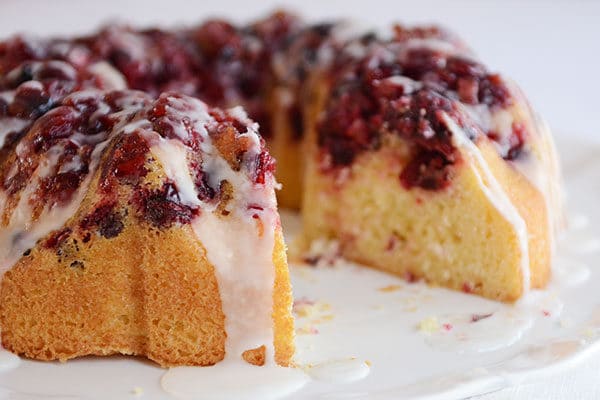 A glazed cranberry lemon bundt cake with a large piece cut out on a white platter.