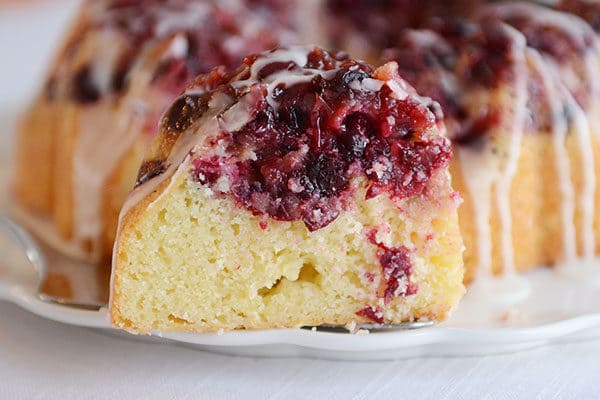 A piece of glazed cranberry lemon bundt cake on a white cake platter.