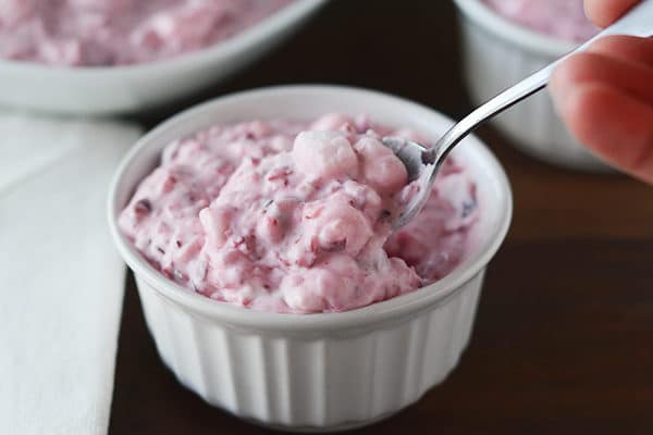 A white ramekin of cranberry fluff salad with a spoon in it.