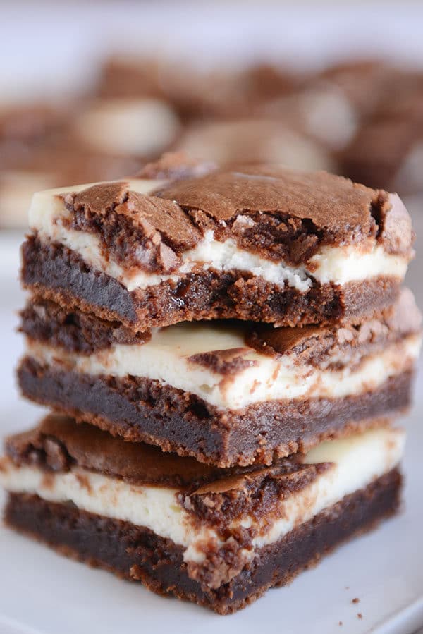 Three cream cheese chocolate brownies stacked on top of each with the top one with a bite taken out.