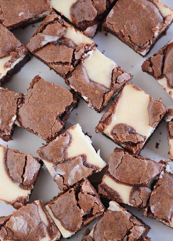 Top view of a bunch of square cream cheese chocolate brownies on a white platter.