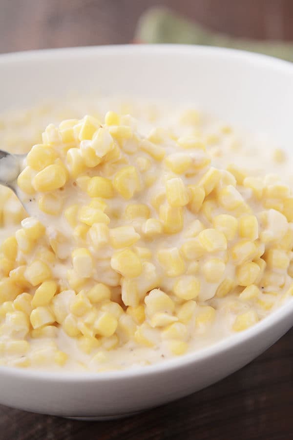 A spoon taking a large scoop of creamy parmesan cream corn out of a white oval bowl.