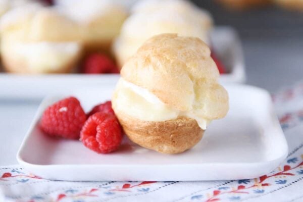 Perfect little foolproof cream puff on white plate with raspberries.