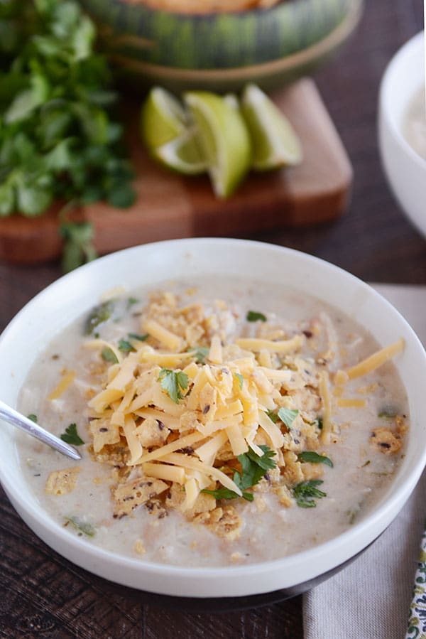 A bowl of white chicken chili with shredded cheddar cheese and cilantro sprinkled on the top.