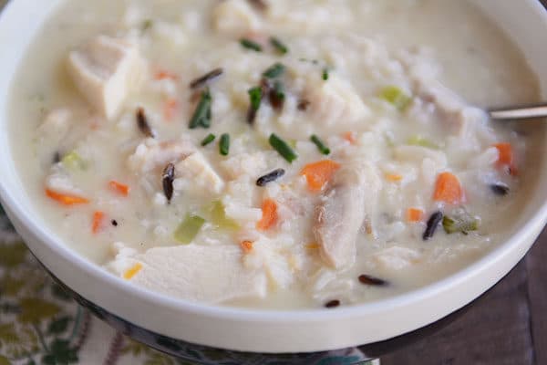 A white bowl of chicken and wild rice soup with a spoon on the side.