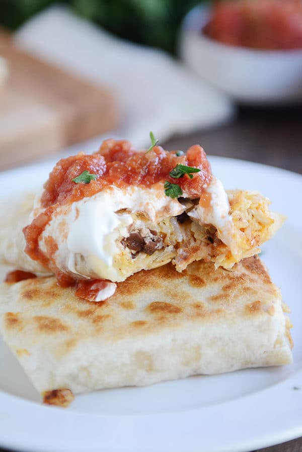 A tortilla sitting on a white plate, filled with southwest ingredients and topped with sour cream, cilantro, and salsa. 