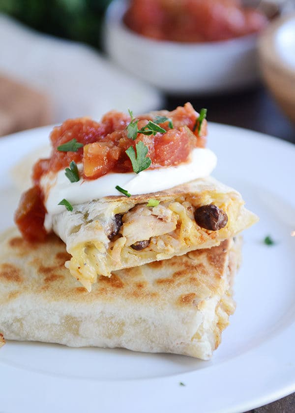 A griddled tortilla sitting on a white plate, filled with southwest ingredients and topped with sour cream, cilantro, and salsa. 