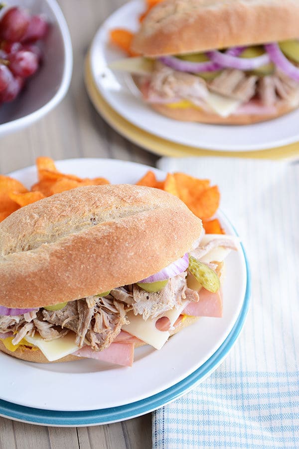 Top view of a Cuban sandwich on a hoagie bun next to a serving of chips on a white plate.