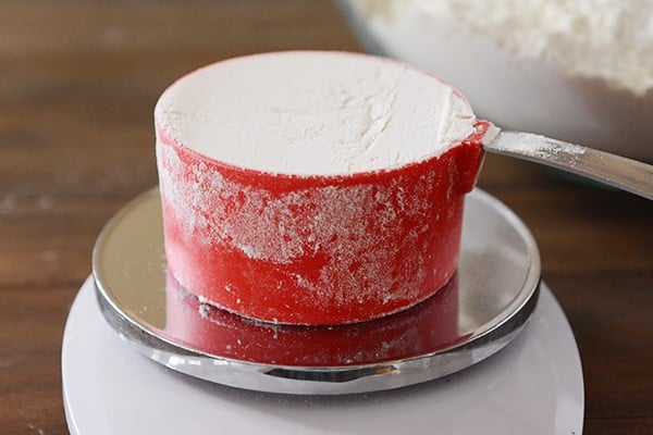 A red measuring cup full of flour sitting on a kitchen scale.