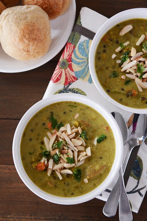 Top view of two white bowls with curry soup topped with almonds and a plate of rolls next to them.