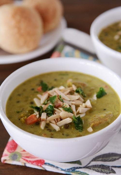 A white bowl of curry lentil soup topped with sliced almonds.