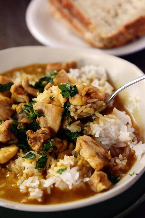 A spoon taking a bite out a bowl of white rice and chicken curry.