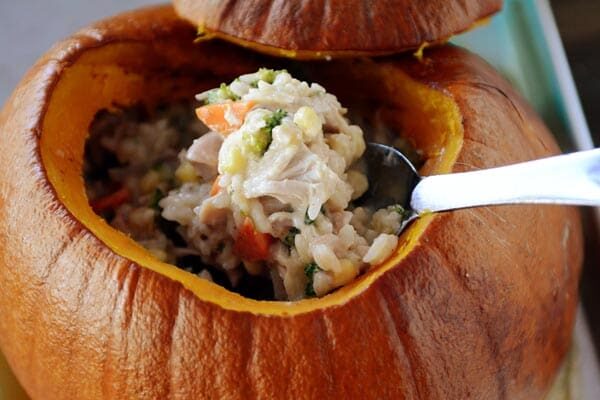 Spoon scooping out casserole from a hollowed out cooked pumpkin. 