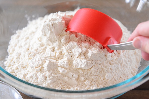 A red measuring cup getting dipped into a bowl of flour.