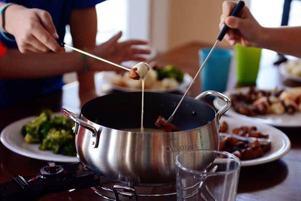 Two people dipping meat into a fondue pot filled with cheese. 