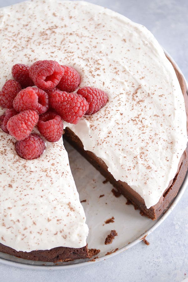 Top view of a whipped cream and raspberry covered chocolate torte with a slice taken out.