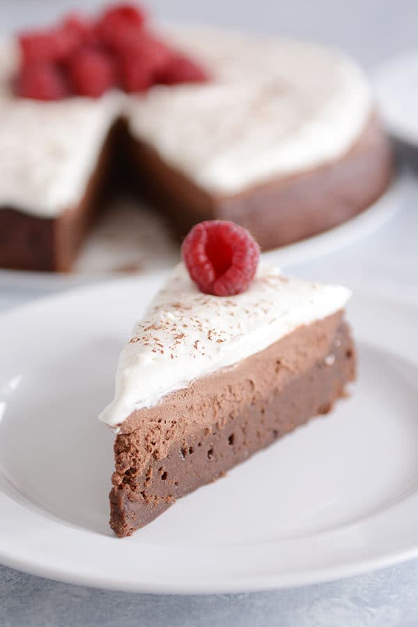 A slice of chocolate mousse torte on a white plate in front of the rest of the torte.