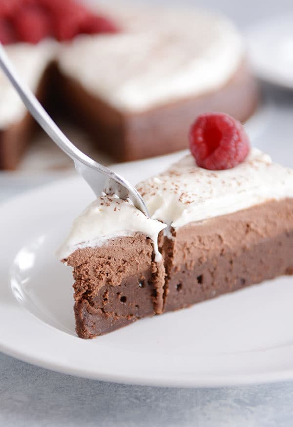 A fork getting a bite off a slice of a double chocolate mousse torte topped with whipped cream.