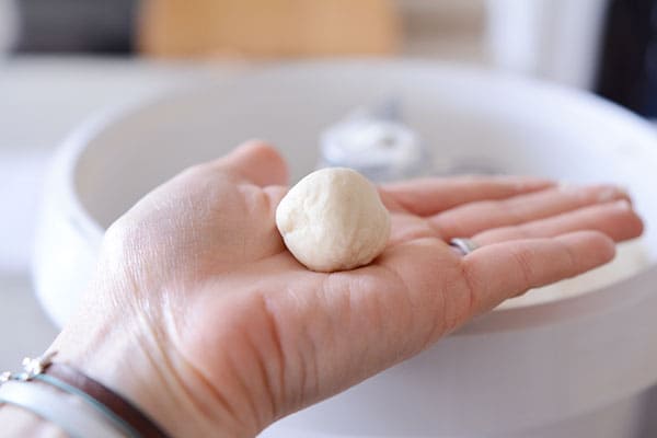 A golf-ball sized piece of white bread dough rolled into a ball, being held on the palm of a hand.