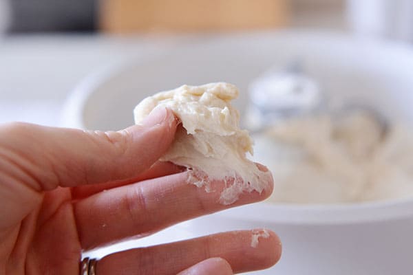 A golf-ball sized piece of bread dough being held between the thumb and middle finger. 