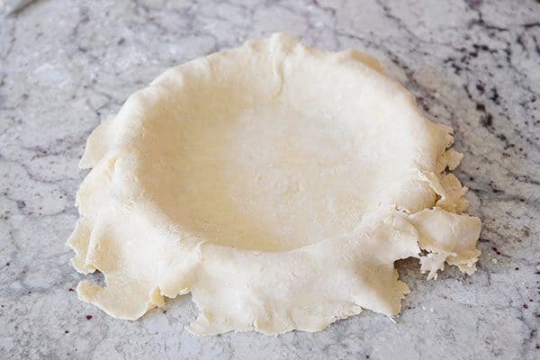 A raw pie crust hanging over the edges of a pie dish.