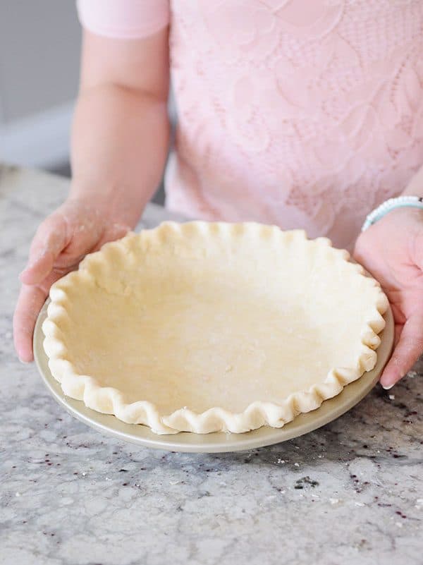 A perfectly crimped raw pie crust getting held by someone in a pink shirt.