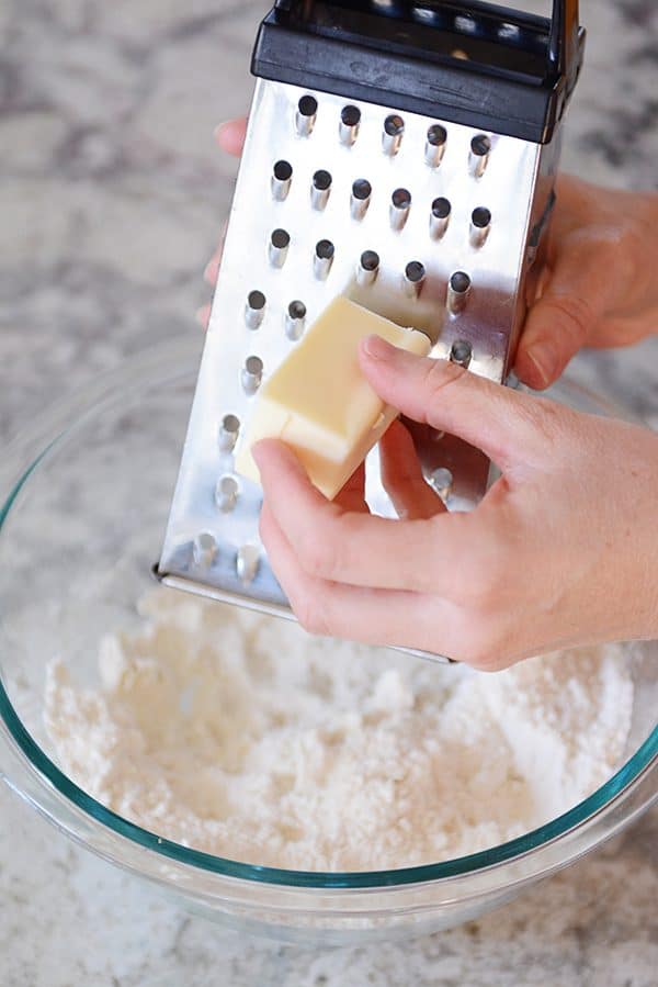 Butter getting grated into a bowl of flour.