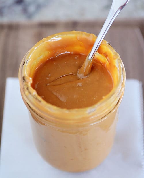 A mason jar full of golden brown dulce de leche with a spoon in it.