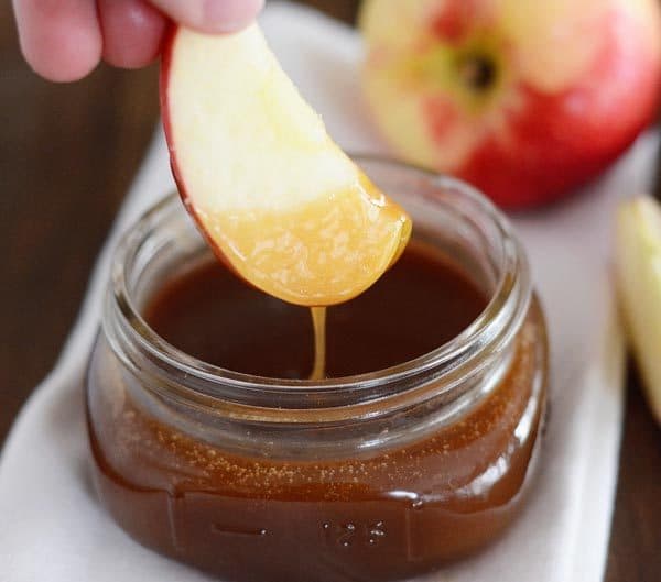 An apple slice dipping into a mason jar of caramel sauce. 