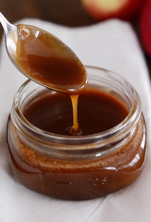 A spoon drizzling caramel sauce into a mason jar of caramel sauce.