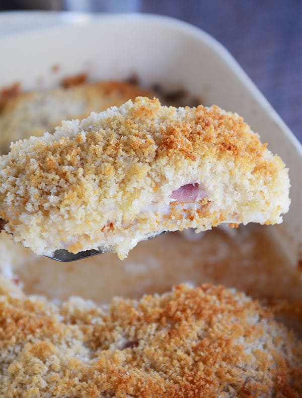 A breaded, chicken cordon bleu being lifted out of a casserole dish.
