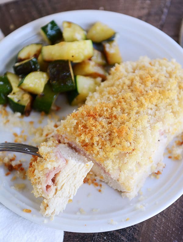 A chicken cordon bleu chicken breast, with a bite being taken out, and sauteed zucchini on the side.