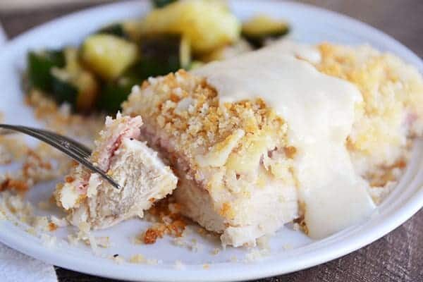 A chicken cordon bleu, with white sauce poured over the top and a bite being taken out.