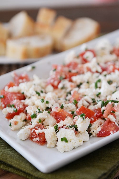 A white tray of Greek feta dip with sliced baguettes in the background.