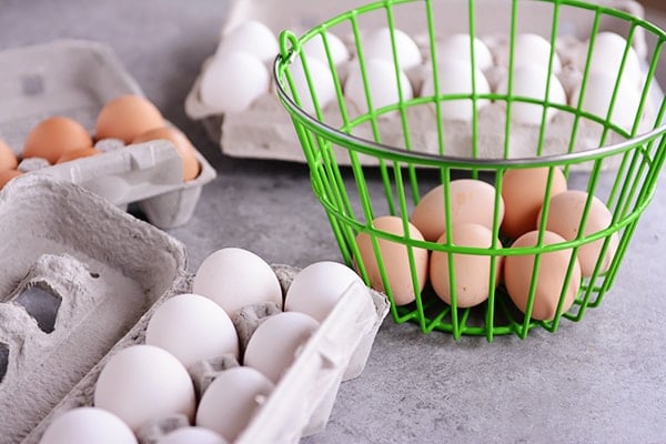 A bunch of raw eggs in cartons and a green basket.