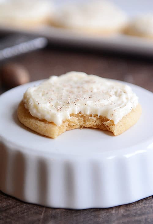 A frosted sugar cookie with a bite taken out on an upside down ramekin.