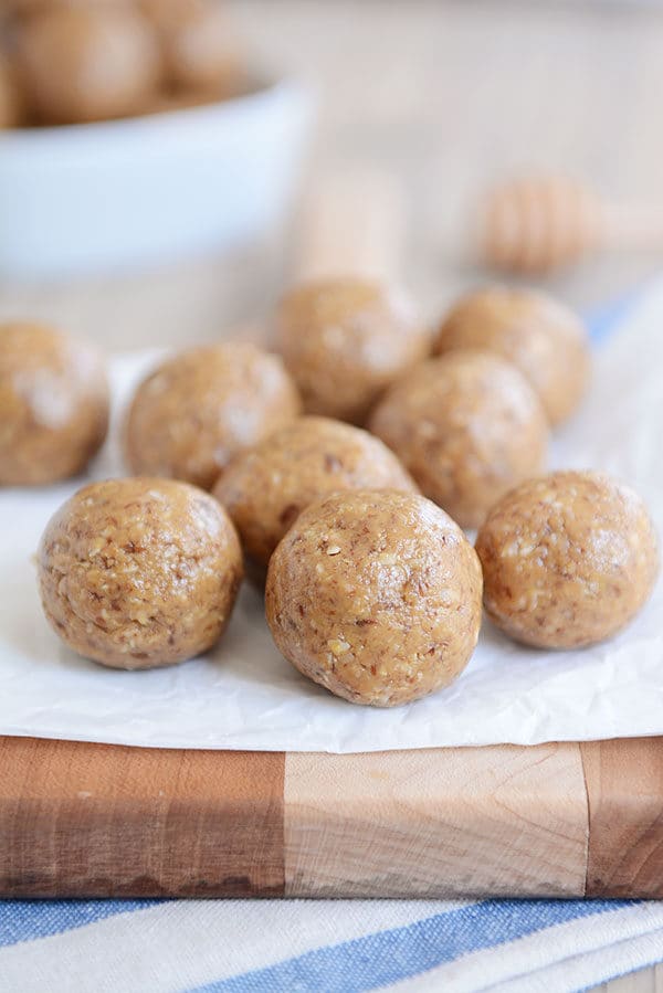 A piece of parchment paper with a nine protein balls and a bowl of more bites in the background.