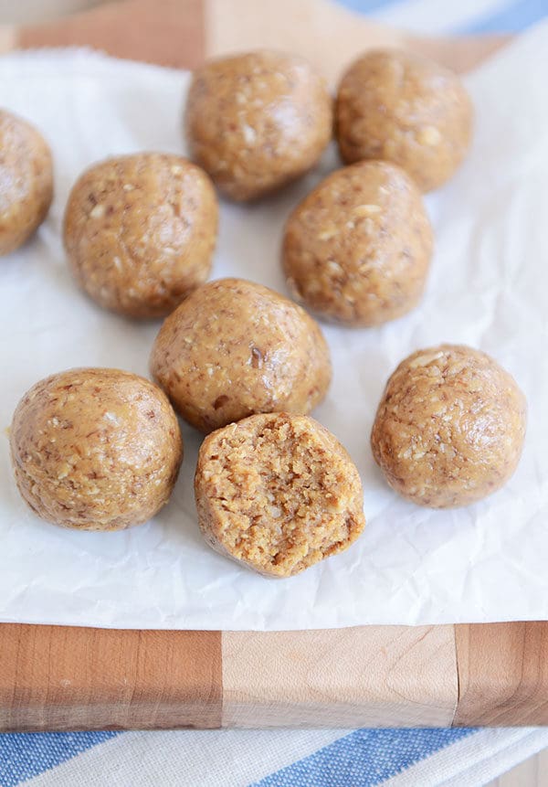 Protein balls on a piece of parchment paper. The one in the front has a bite taken out. 