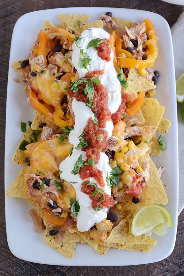 Top view of a white platter of cheesy fajita nachos topped with sour cream and salsa.