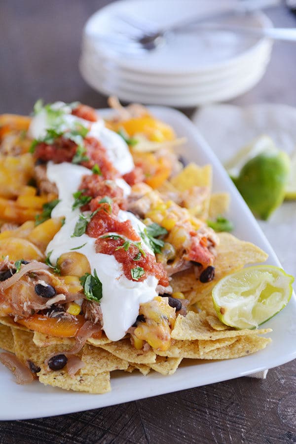 A white platter full of cheesy fajita nachos and toppings.