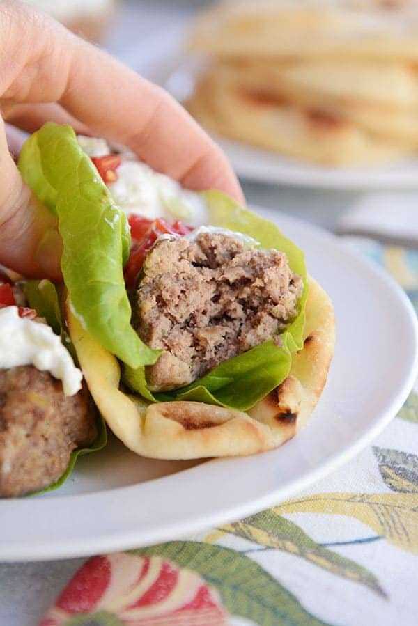 A falafel meatball with a bite taken out on a flatbread with lettuce and tzatziki sauce.